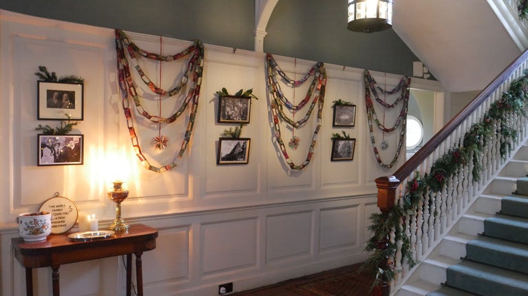 A wall is decorated with paper chains with a staircase in the foreground covered in evergreen branches